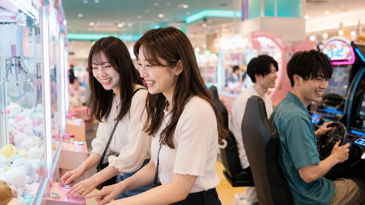 明るいアミューズメント施設で、若者グループがゲームやアトラクションを楽しんでいる様子